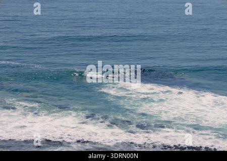 Hochwinkelaufnahme von türkisfarbenen Wellen, die über einem felsigen Riff in Iquique, Chile, in weißen Schaum einbrechen und Bewegung und Textur zeigen Stockfoto