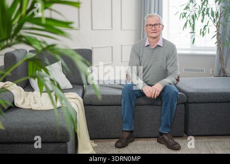 Porträt eines selbstbewussten, stilvollen europäischen Seniorenmannes mittleren Alters zu Hause. Älterer reifer Mann der 70er Jahre lächelt. Glückliche attraktive Seniorengra Stockfoto