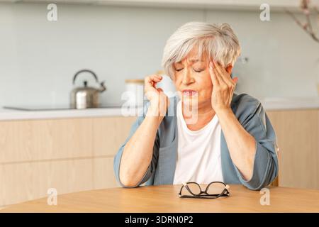 Kopfschmerzen, unglückliche Seniorin mittleren Alters, die an Kopfschmerzen leidet, krank, die Schläfen zu Hause reibt. Reifer alter Seniorengroßmot Stockfoto