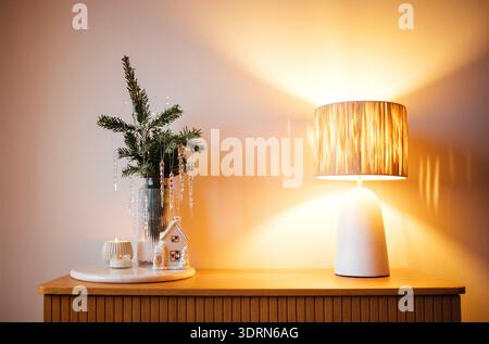 Gemütliche Inneneinrichtung mit dekorativer Lampe, kleiner immergrüner Pflanze und Kerze auf einem Holztisch, die eine warme und einladende Atmosphäre schaffen Stockfoto