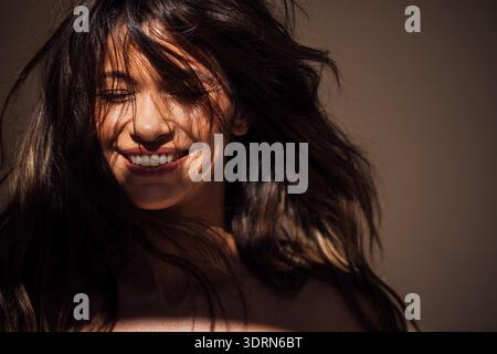 Lächelnde Frau mit fließenden Haaren, die von sanftem Licht beleuchtet werden und fröhlichen Ausdruck und natürliche Schönheit in einer ruhigen Umgebung zeigen Stockfoto