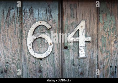 Verwittertes Haus Nr. 64 auf einer alten Holzoberfläche Stockfoto