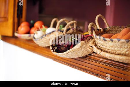 Bunte Auswahl an frischem Gemüse und Obst in gewebten Körben, die auf einer Holzarbeitsfläche angeordnet sind, mit leuchtenden Farben A Stockfoto