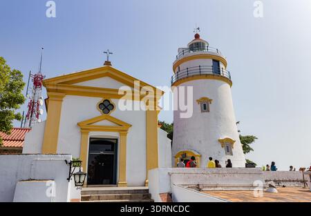 Weißer Leuchtturm und Kapelle mit Touristen am sonnigen Tag in der Nähe des roten Kommunikationsturms. Stockfoto