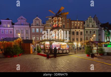 Festlicher Abendblick auf Weihnachtsmarkt Stände und beleuchtete Windmühle auf dem Alten Marktplatz in Posen, Polen. Historische farbenfrohe Stadthäuser im B Stockfoto