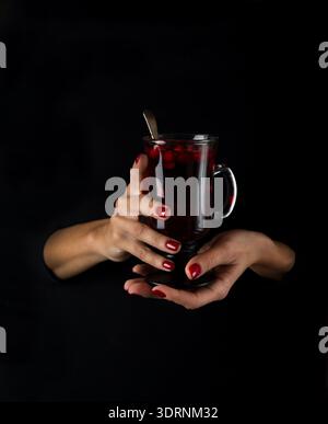 Weibliche Hände halten Glas mit heißem Preiselbeertee Stockfoto