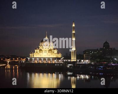 Atemberaubender Blick bei Nacht auf die beleuchtete Putra Moschee (Rosa Moschee) in Putrajaya, Malaysia. Mit ruhigen Reflexen des Sees und leuchtend rosa Kuppeln. Stockfoto