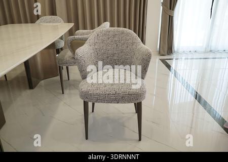 Stuhl mit gemustertem Stoff steht vor einem Tisch. Der Stuhl befindet sich vor einem Fenster, das natürliches Licht einlässt. Das Zimmer hat einen Modus Stockfoto