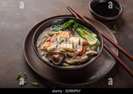 Asiatische vegane Nudelsuppe mit Tofu-Käse, Shiitake-Pilzen und pak Choi, dunkler Hintergrund Stockfoto