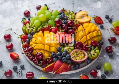 Köstliche Platte mit Früchten und Beeren. Mango, Kiwi, Erdbeere, Traube, Kirsche, Heidelbeere, Pfirsich und Passionsfrucht Stockfoto
