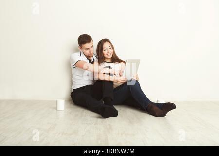 Ein Paar sitzt zusammen auf dem Boden, während es sich ein Tablet in einem einfachen Innenraum ansieht Stockfoto