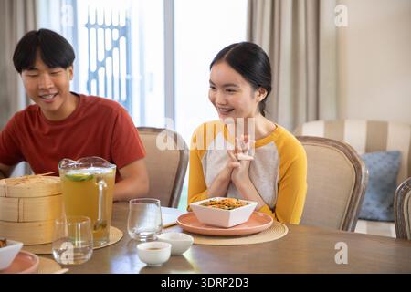 Asiatisches Paar sitzt zu Hause am Esstisch mit Nudelsalat, Bambusdampfer und Eistee. Restaurant, Restaurant, gemütlich, modern, l Stockfoto