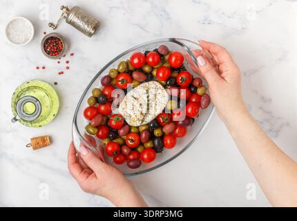 Eine Frau hält eine Glasplatte mit weißem Schimmelkäse (Camembert, Brie), Kirschtomaten, schwarzer und grüner Olive in den Händen Stockfoto