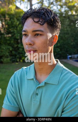 Asiatischer Mann, der im Garten unter Sonnenlicht steht, hellgrünes Poloshirt trägt, nach links gerichtet. Outdoor, Freizeit, Ruhe, Natur, Stockfoto