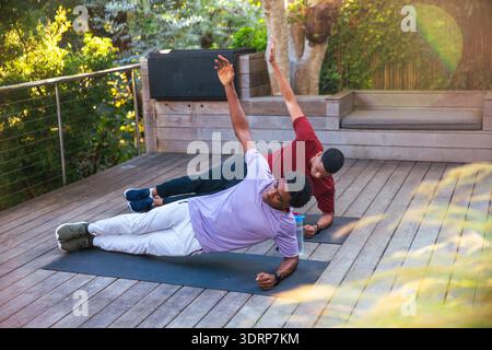 Afroamerikanische Männer, die Seitenplanken auf dem Hinterhof mit Yogamatten und Wasserflasche spielen. Fitness, Wellness, Kraft, Outdo Stockfoto