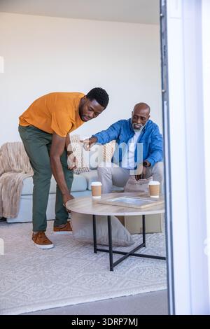 Afroamerikaner Vater und Sohn nehmen Kissen neben Kaffeetassen auf dem Wohnzimmertisch. Familie, Zuhause, Bindung, Entspannung, Stockfoto