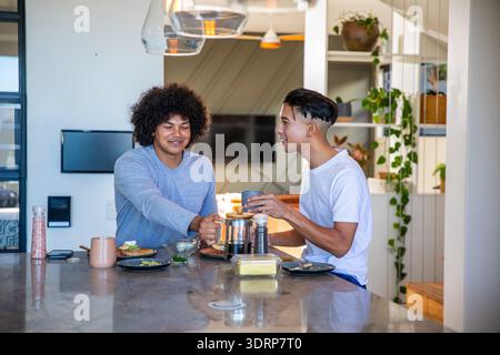 Verschiedene männliche Freunde, die auf der Kücheninsel French Press Kaffee gießen und sich bei Avocado Toast unterhalten. Kameradschaft, lässig, besinnlich Stockfoto