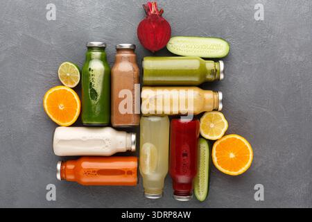 Frische Säfte auf grauem Hintergrund mit verstreuten Früchten und Gemüse Stockfoto