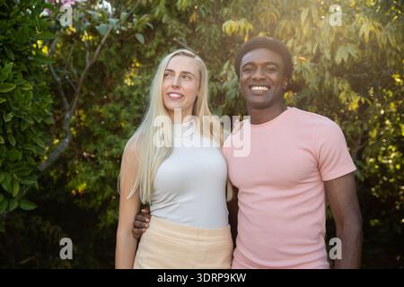 Verschiedene Paare stehen im sonnendurchfluteten Garten mit weißem Oberteil, leichtem Rock und blassrosa Hemd. Romantik, Zuneigung, Gelassenheit, Intim Stockfoto