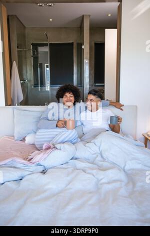 Verschiedene Männer sitzen auf dem Bett in einem Glasduschkabine mit Keramikbecher und Federdecke. Entspannung, Intimität, Komfort, s Stockfoto