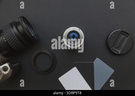 Fotograf-Arbeitsplatz mit dslr-Kamerasystem, Kamerareinigungskit, Objektiv und Kamerazubehör auf dunkelschwarzem Tischhintergrund. H Stockfoto