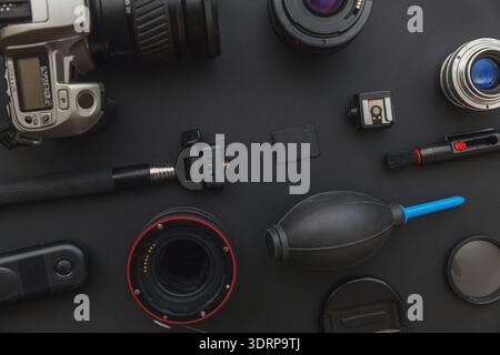 Fotograf-Arbeitsplatz mit dslr-Kamerasystem, Kamerareinigungskit, Objektiv und Kamerazubehör auf dunkelschwarzem Tischhintergrund. H Stockfoto