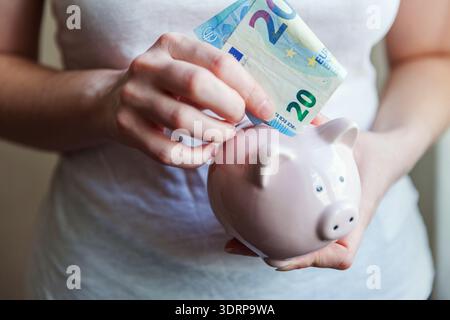 Weibliche Hände halten rosa Schweinebank und geben Geld Euro. Einsparung von Investitionsbudget Geschäftsvermögen Altersvorsorge finanziell Stockfoto