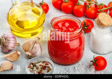Traditionelle Tomatensauce in einem Glas mit Knoblauch und Gewürzen. Zutaten und Olivenöl auf die helle Oberfläche. Selektiver Fokus Stockfoto