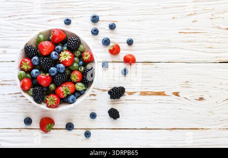 Frische saftige, reife Beeren in einem weißen Teller - Erdbeeren, Heidelbeeren, Brombeeren und Stachelbeeren Stockfoto