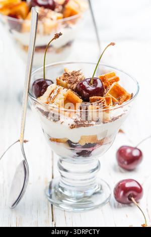 Dessert mit Waffeln, Frischkäse (Ricotta, Mascarpone, Joghurt) und frischen Kirschen mit Schokoladenchips im Glas. Köstliches gou Stockfoto