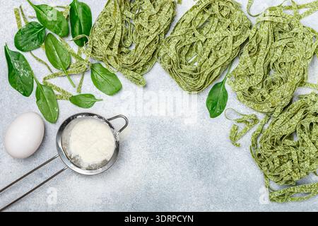 Rohe hausgemachte italienische grüne Pasta Tagliatelle. Trockene Nudeln und Zutaten (Spinat, Mehl, Ei). Selektiver Fokus, Draufsicht, Kopieren Stockfoto