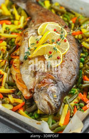 Gebackene Fischforelle mit Gemüse (Kartoffeln, Karotten, Bohnen, grüne Erbsen und Zwiebeln) mit Zitrone, Thymian und rosa Pfeffer. Wil Stockfoto