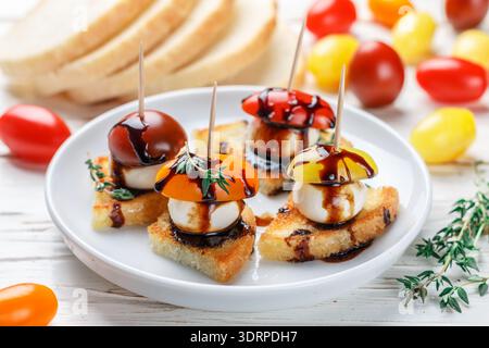 Toast mit Tomatenkirsche, Mozzarella, Thymian und Balsamico auf weißem Holzhintergrund. Canape. Bruschetta. Gour Stockfoto