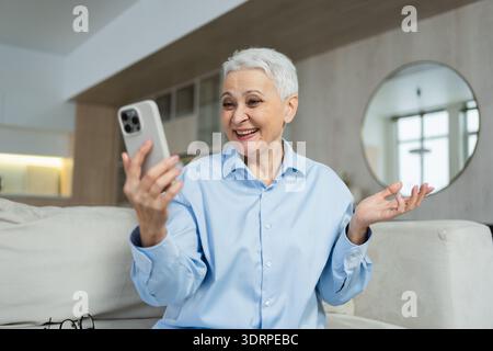 Glückliche ältere Frau mittleren Alters, die mit dem Smartphone bei Videoanrufen mit Freunden und Familie spricht. Lachende alte Seniorin Oma Stockfoto
