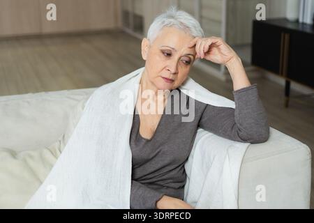 Traurig müde krank krank einsam enttäuschte ältere Frau, die allein zu Hause sitzt. Unglückliche reife Großmutter mit Trauer r Stockfoto