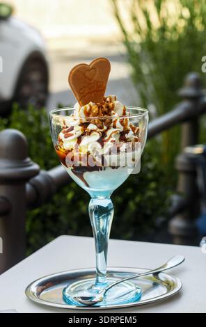 Dessert aus Eis, Schlagsahne, Walnüssen und Karamell (Ahornsirup) in einem hohen blauen Glas in einem Straßencafé. Selektiver Fokus Stockfoto