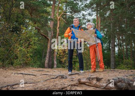 Wandertourismus. Senior Paar Mann Frau, die auf einer Karte auf Papier sucht, genießt Wanderungen im Wald. Glückliche alte Leute, die Rucksacktouristen wandern Stockfoto