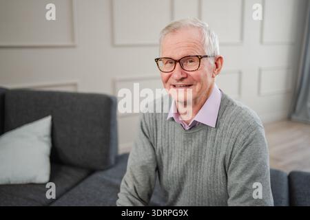 Porträt eines selbstbewussten, stilvollen europäischen Seniorenmannes mittleren Alters zu Hause. Älterer reifer Mann der 70er Jahre lächelt. Glückliche attraktive Seniorengra Stockfoto