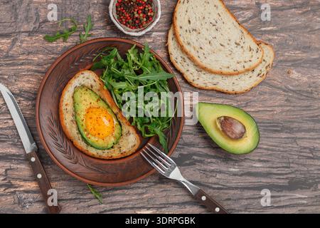 Geröstetes Vollkornbrot mit Leinsamen mit Avocado, Ei, Gewürzen und Gewürzen auf einer braunen Platte auf hölzernem Hintergrund. Serv Stockfoto