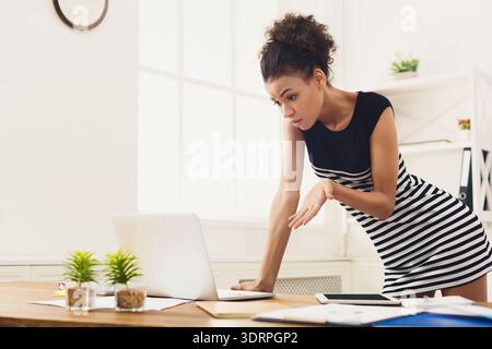 Frau, die einen Laptop benutzt, während sie überrascht aussieht und in einem hellen Bürobereich Gesten macht Stockfoto