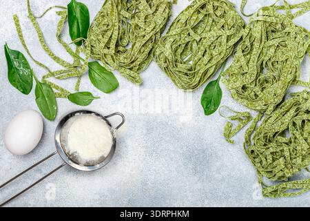 Rohe hausgemachte italienische grüne Pasta Tagliatelle. Trockene Nudeln und Zutaten (Spinat, Mehl, Ei). Selektiver Fokus, Draufsicht, Kopieren Stockfoto