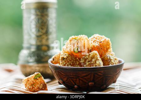 Traditionelles türkisches Vergnügen. Lokum. Orientalische Süßigkeiten mit Sesam und Pistazien in einer Keramikschale auf dem Tisch. Ein Genuss für Tee. Stockfoto