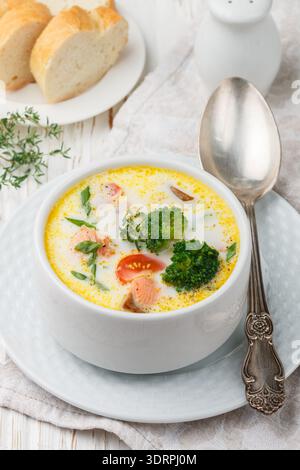 Fischsuppe mit Kartoffeln, Karotten, Tomaten und Brokkoli in einer weißen Schüssel auf hellem Holztisch Stockfoto