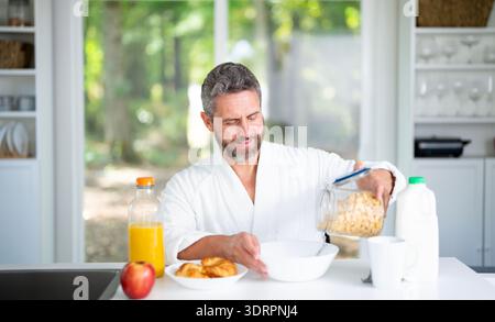Der Mann frühstückt morgens in der Küche. Der Mann genießt eine gesunde Mahlzeit am Küchentisch. Ein Mann isst Müsli und Obst in der Küche Stockfoto