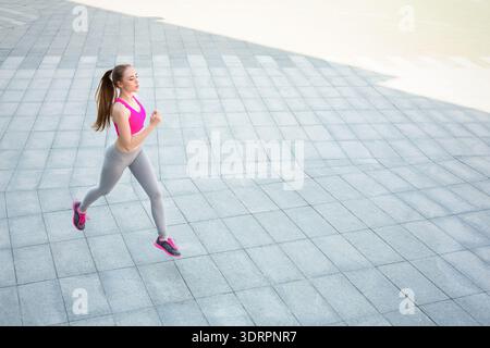 Läufer in Bright Workout Ausrüstung joggt tagsüber auf glattem Gehweg in Urban Area Stockfoto