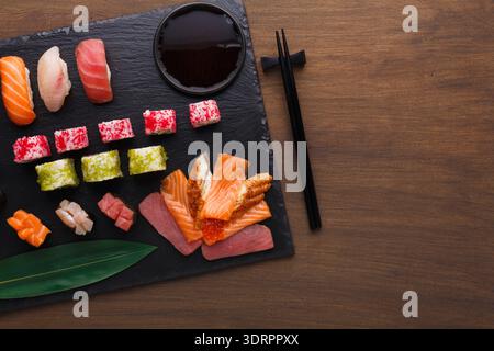 Verschiedene Sushi-Stücke auf einem schwarzen Schieferteller mit Sojasauce und Essstäbchen Stockfoto