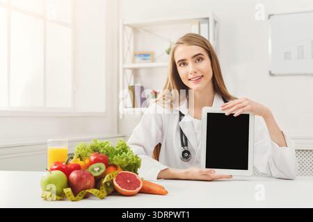 Healthcare Professional zeigt ein digitales Tablet mit gesunden Lebensmitteln in einem hellen Büro Stockfoto