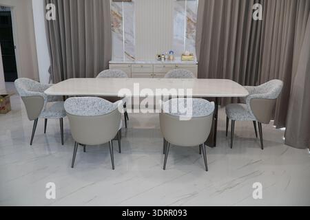 Langer weißer Esstisch mit sechs Stühlen. Die Stühle sind alle weiß und haben ein Muster. Der Tisch ist für eine Mahlzeit gedeckt, mit einer Schüssel und einer Stockfoto