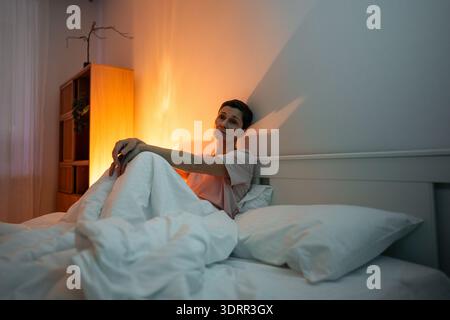 Erschöpfte, nachdenkende Seniorin mit Schlaflosigkeit Schlafstörung im Bett sitzend mit müdem Ausdruck. Stockfoto