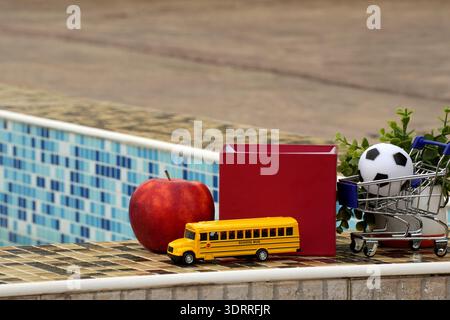 Back-to-School-Konzept mit Apfelbuch-Spielzeugbus und Miniwagen, die den unterkonsumierten Kernlokalismus symbolisieren, das Einkaufen und die Bildungswirtschaft Stockfoto